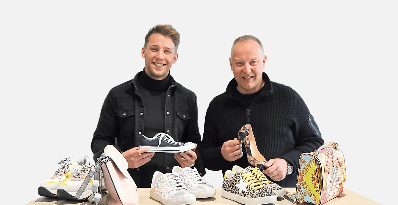 Zwei Mitglieder des Heinmüller Teams mit Sneakern, Damenschuhen und Taschen